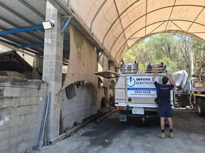Infuse Electrical electrician loading ladders onto the branded service ute under a large arched canopy at a Mackay depot